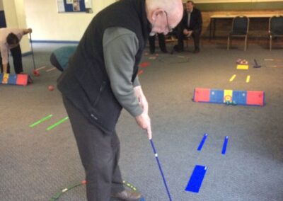 Older man putting ball on a carpet towards a target.