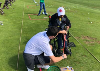 Coach teaching man in wheelchair to hit a golf ball on a driving range