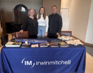 2 women and a man stand in front of a table with Irwin Mitchell logo on with brochures on the table.